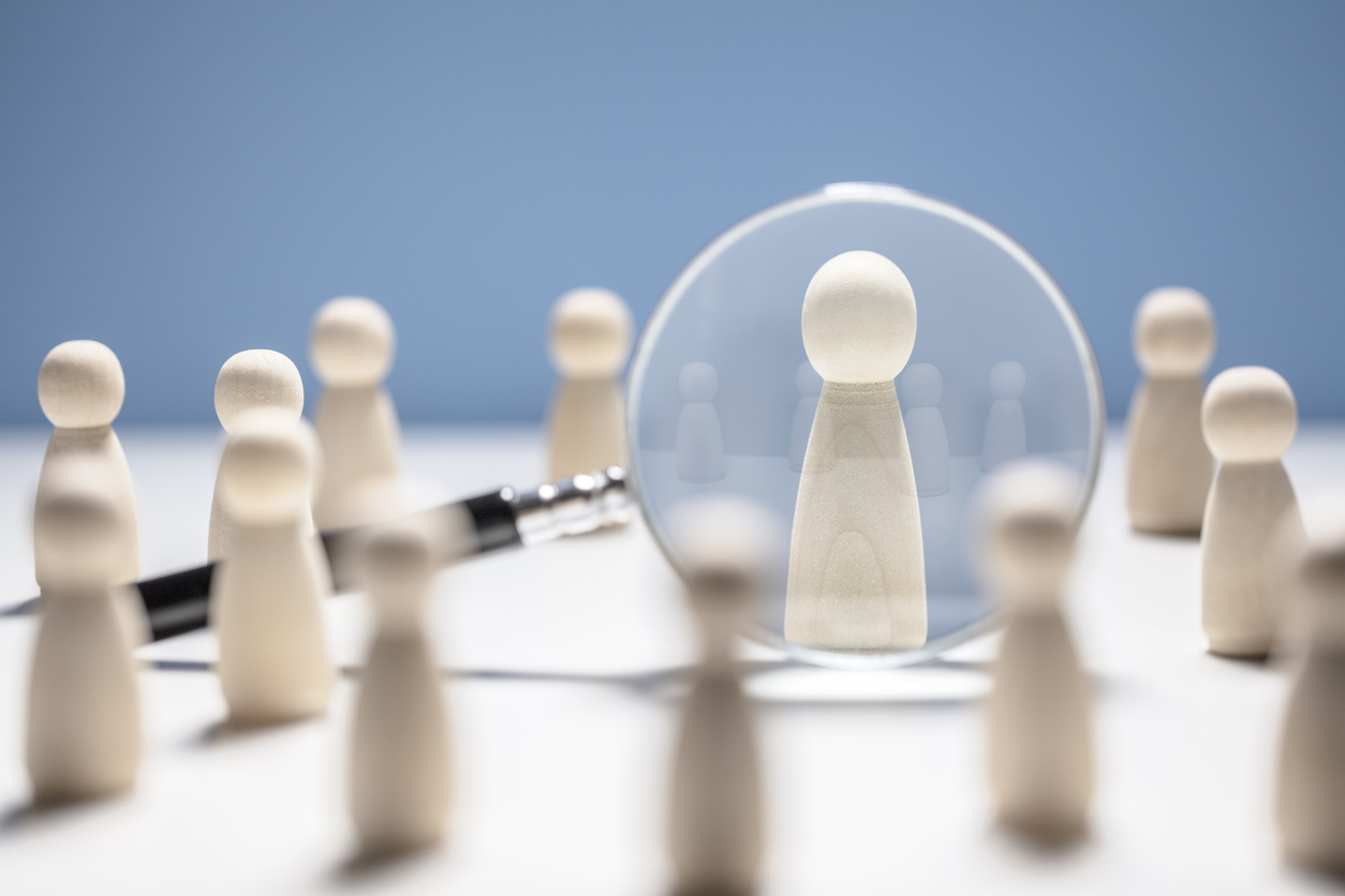 Wooden people with one viewed through a magnifying glass