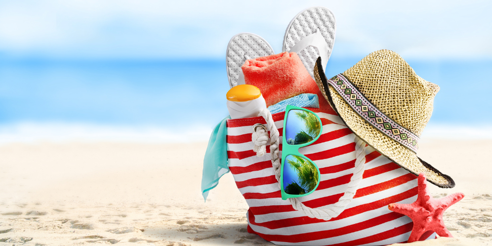 Beach bag on sandy beach filled with holiday essentials.